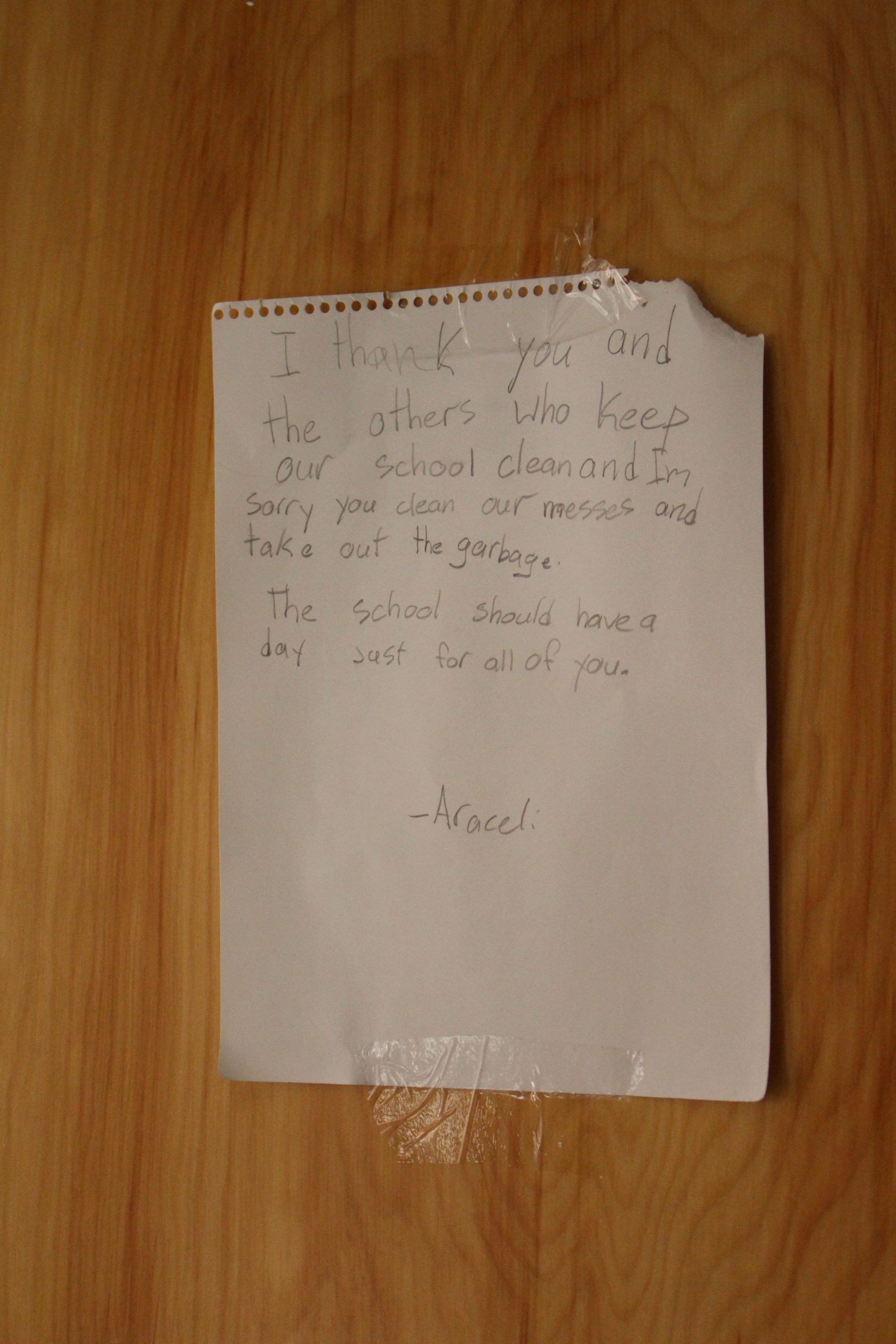 photo is of a note taped to a door. The note is on looseleaf paper torn from a notebook and reads: “I thank you and the others who keep our school clean and I’m sorry you clean our messes and take out the garbage. The school should have a day just for all of you.” 