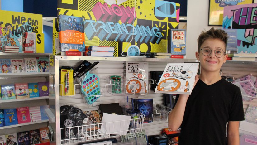 a pre-teen boy is holding up a book and smiling.