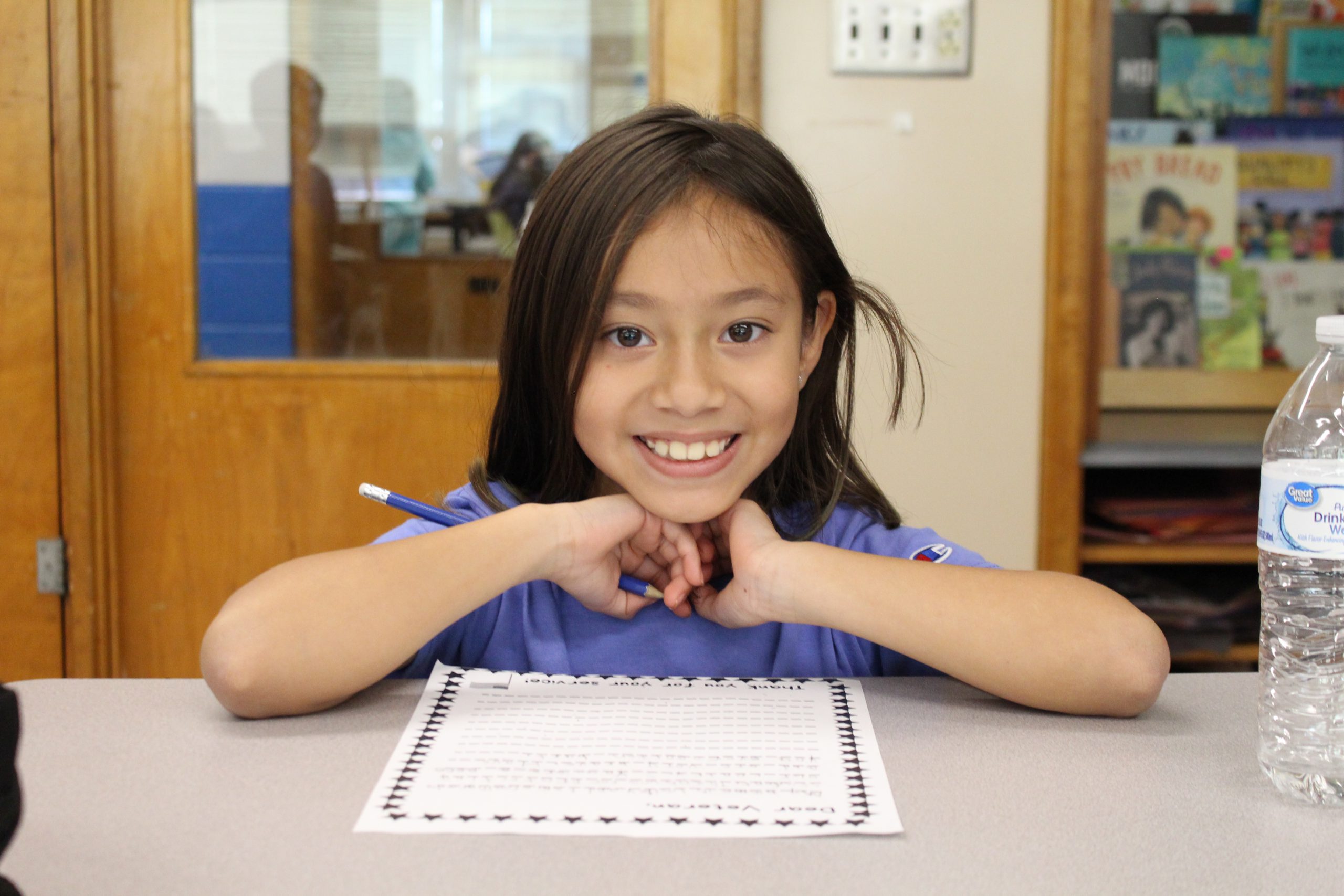 a girl is seated at a desk writing a letter.