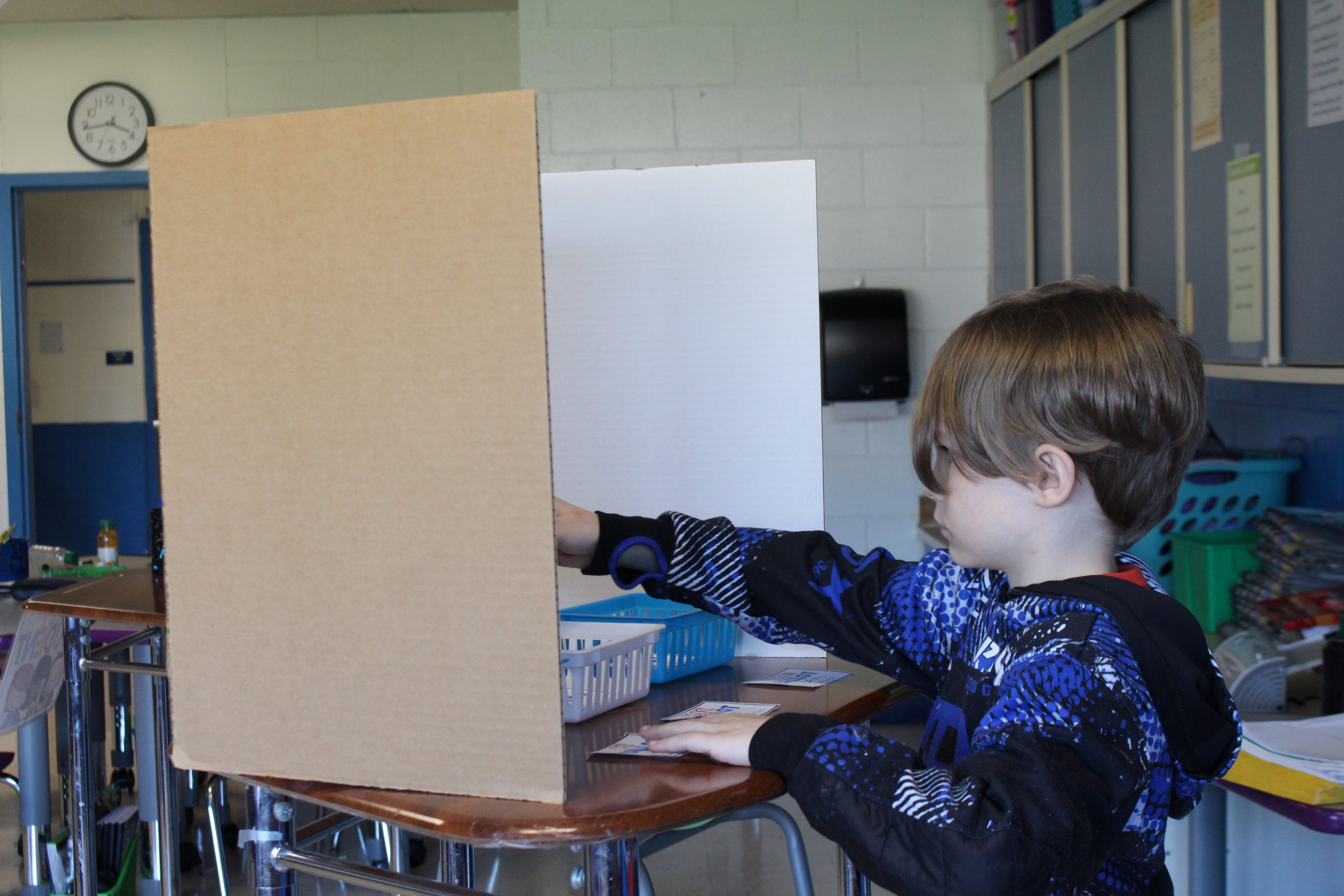 a student is standing at a table. It is meant to look like a privacy shield at a polling site. 