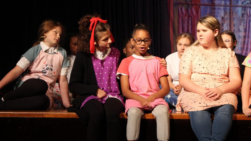 a group of young girls are sitting on stage during a performance.