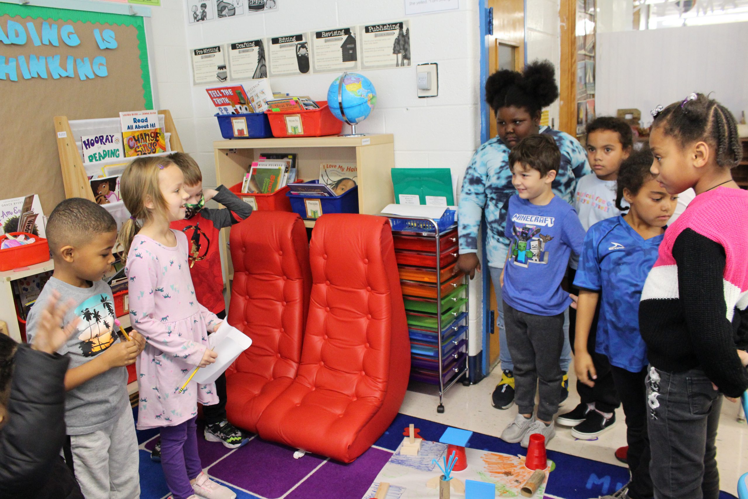 two students are standing in front of another group of students. They are facing one another, and the two students are in the middle of presenting to the other group. 