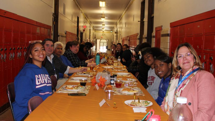 a large group of people are seated at a long table. The table is decorated in autumn colors