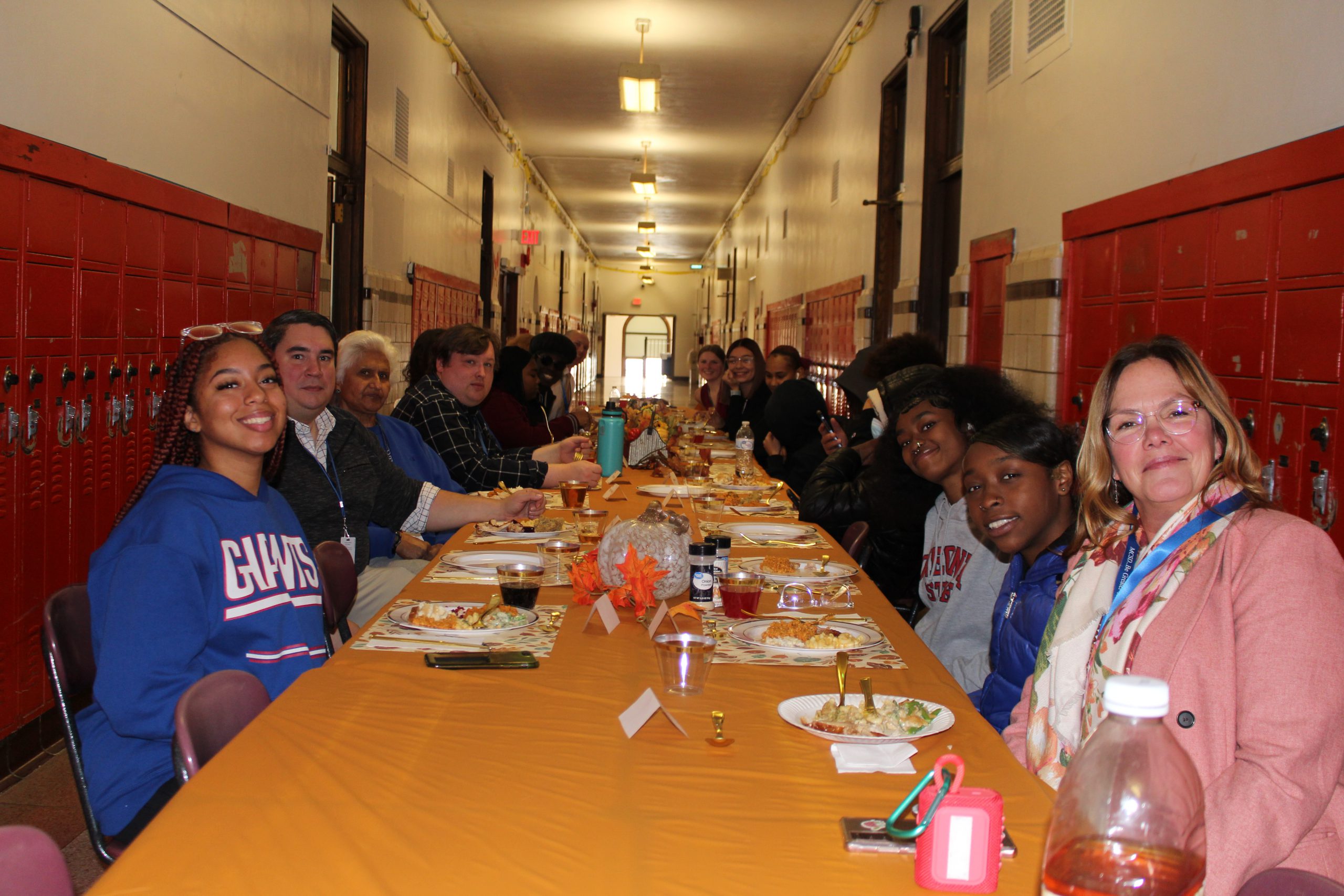 a large group of people are seated at a long table. The table is decorated in autumn colors 