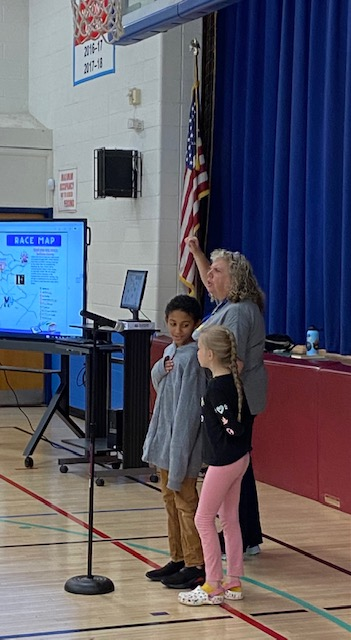 A woman is standing in front of a microphone with two children next to her