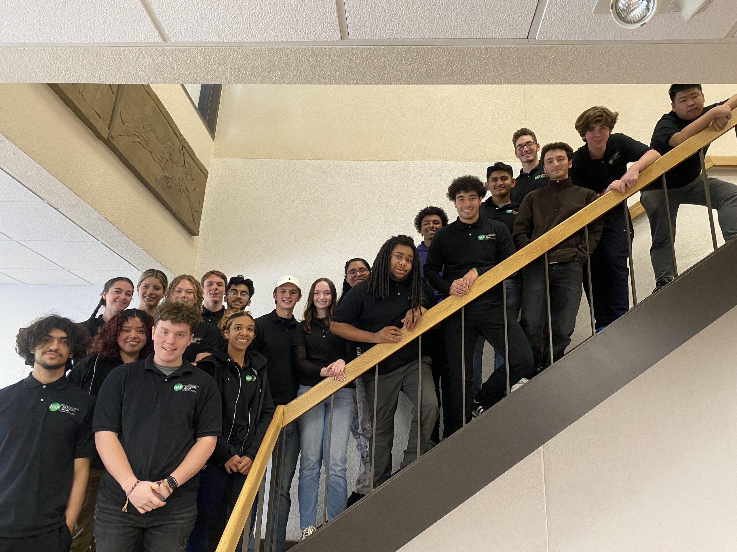 a group of students wearing Academy of Finance tshirts are posing on a staircase. 