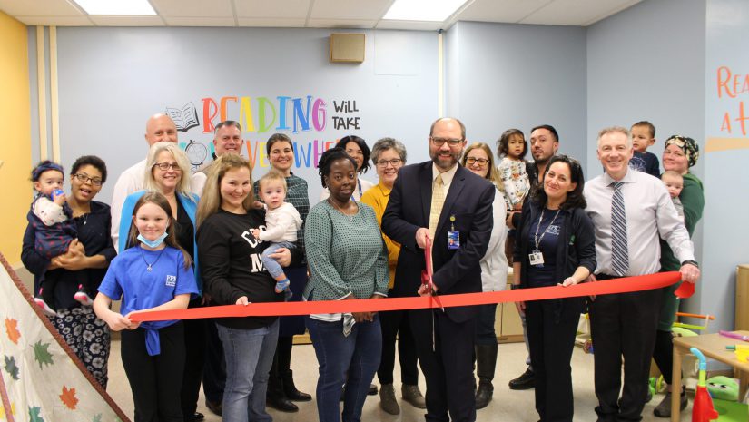 A group of people are posing and in the middle of cutting a ribbon.