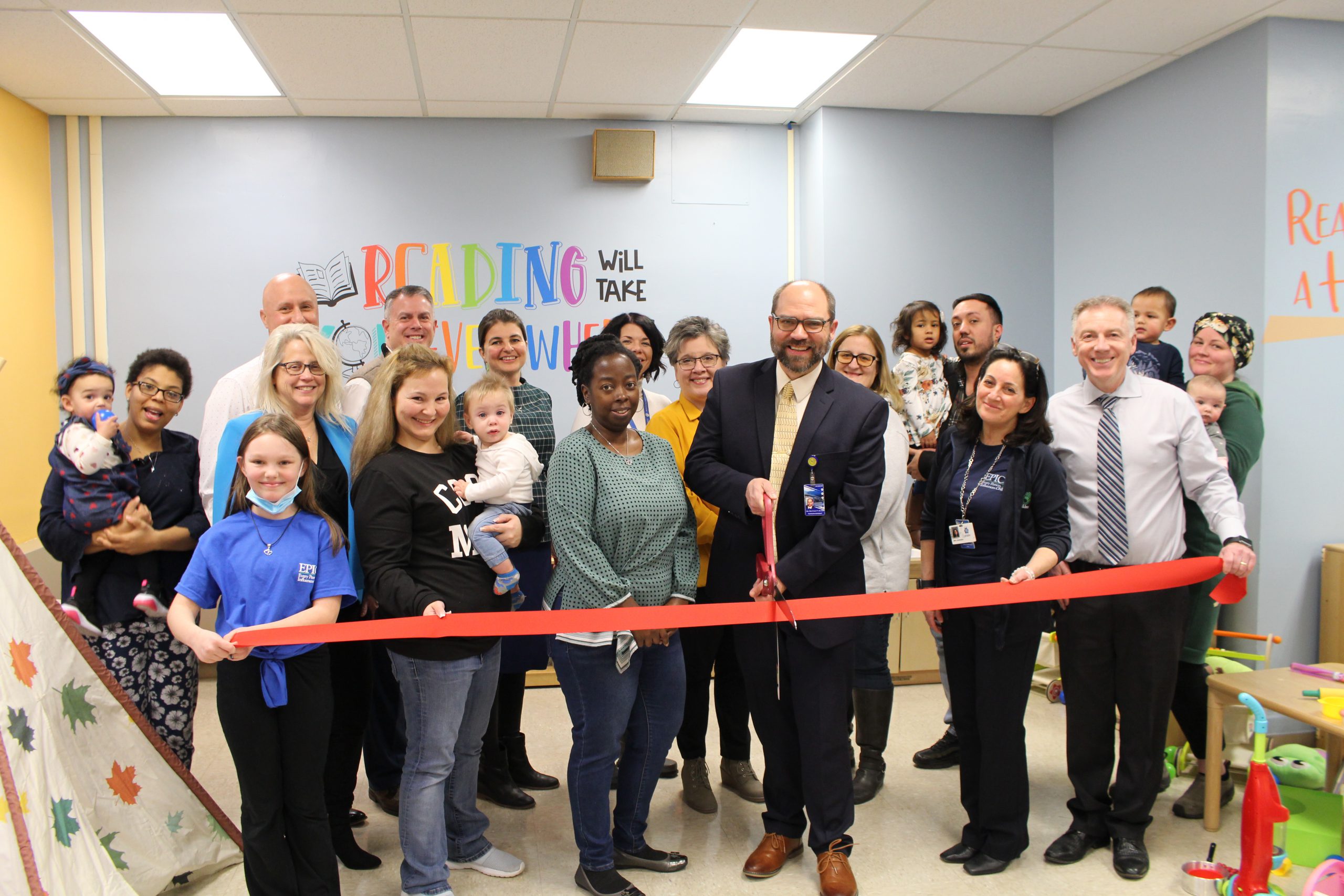 A group of people are posing and in the middle of cutting a ribbon. 