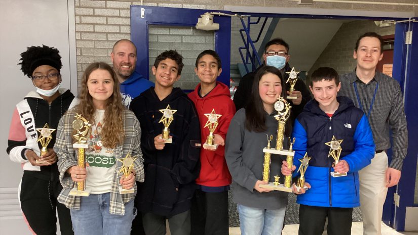 Students and teachers from the math team are posing, and holding up trophies