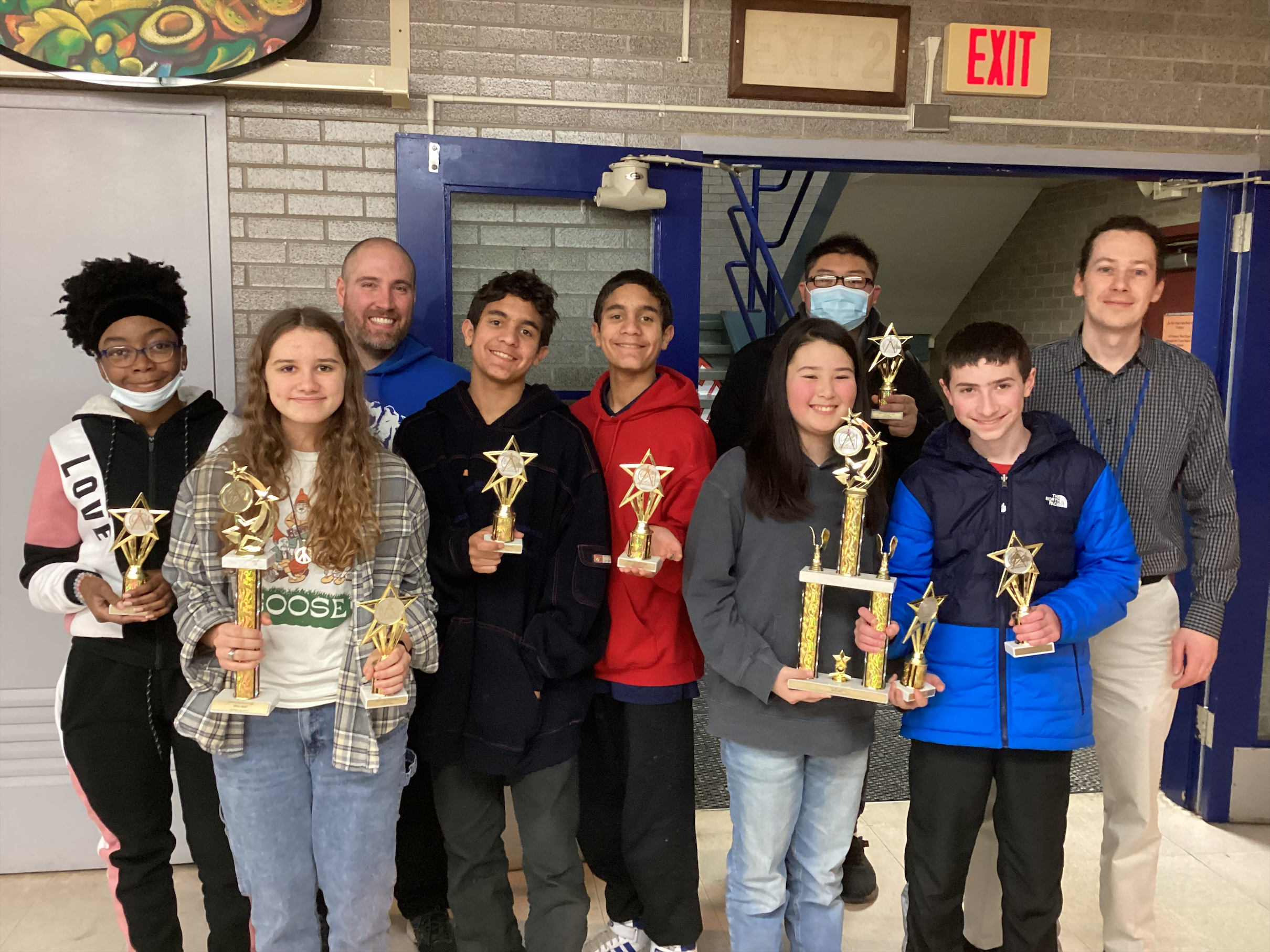 Students and teachers from the math team are posing, and holding up trophies 