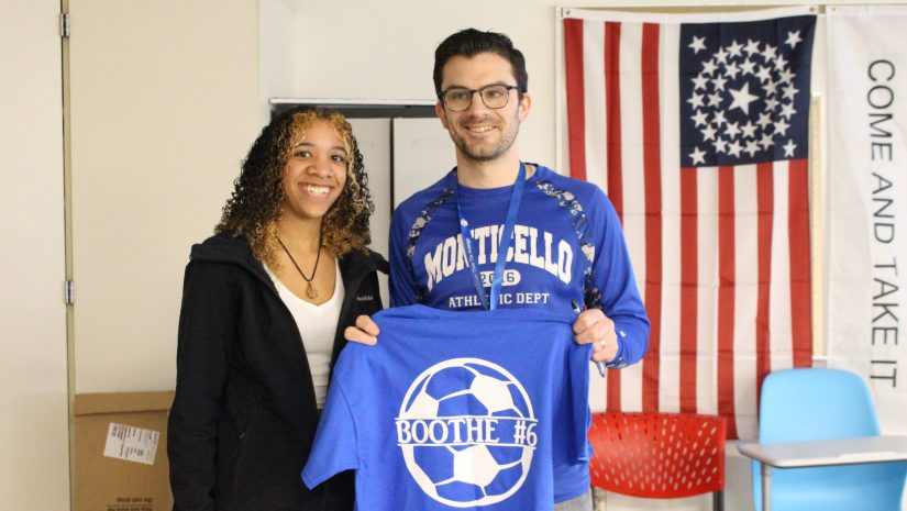 a student is posing with a teacher who is holding up a tshirt.