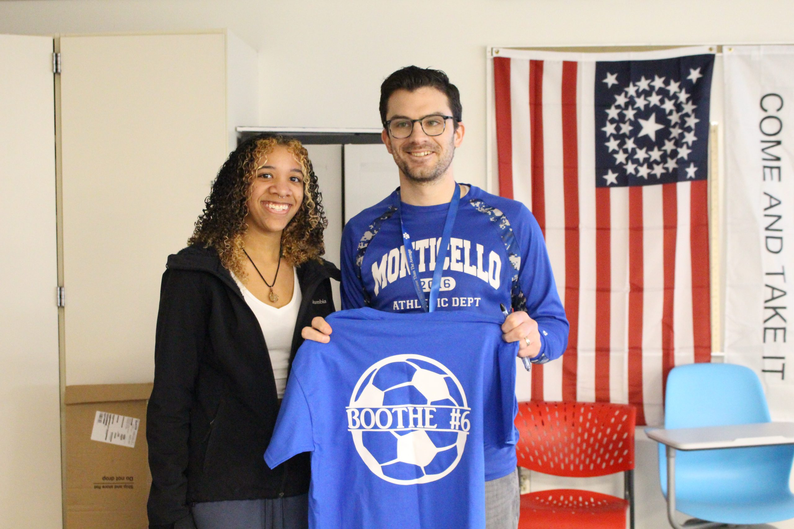 a student is posing with a teacher who is holding up a tshirt.