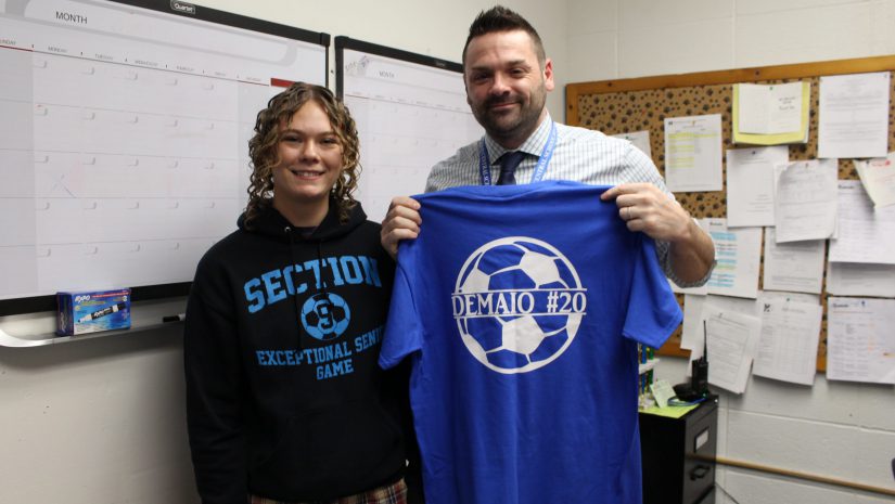 a student is posing with a teacher who is holding up a tshirt