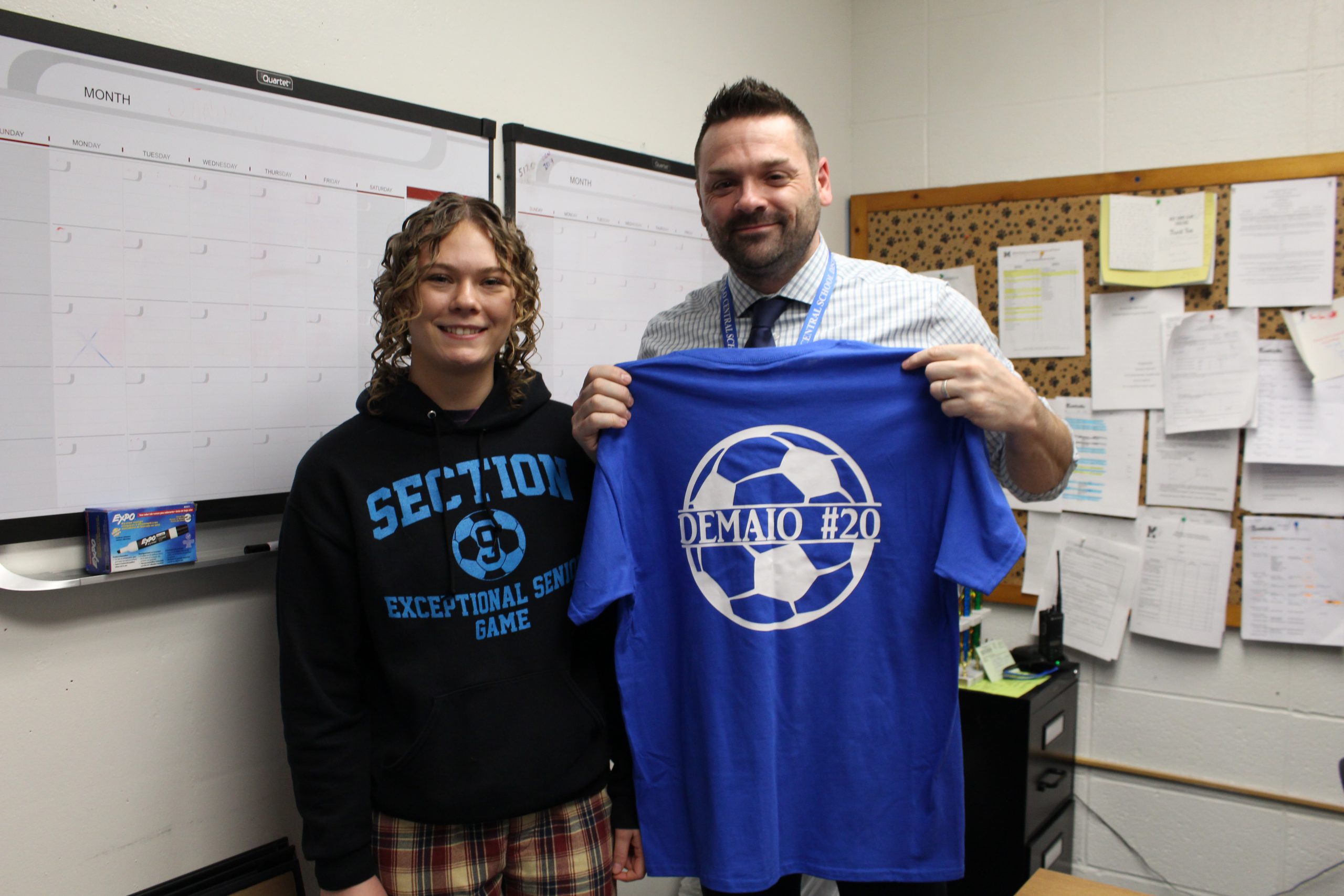 a student is posing with a teacher who is holding up a tshirt