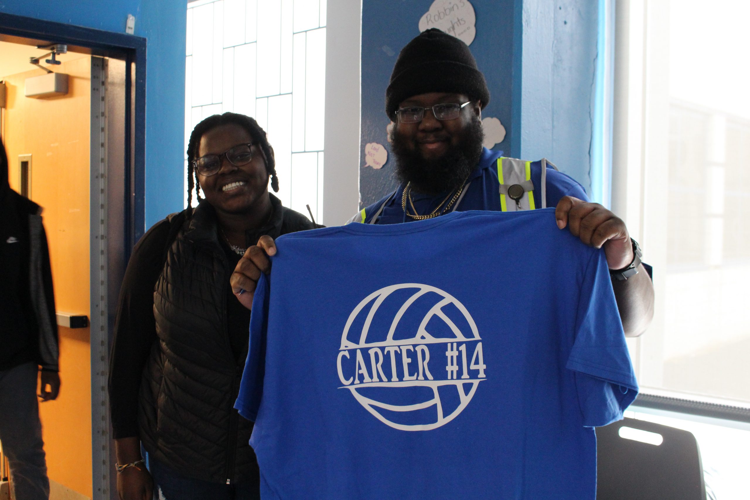 a student is posing with a security guard, who is holding up a tshirt. 