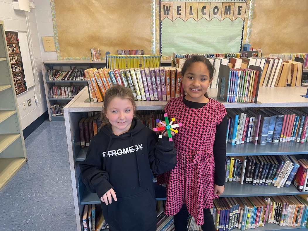 two students pose holding a snowflake they created