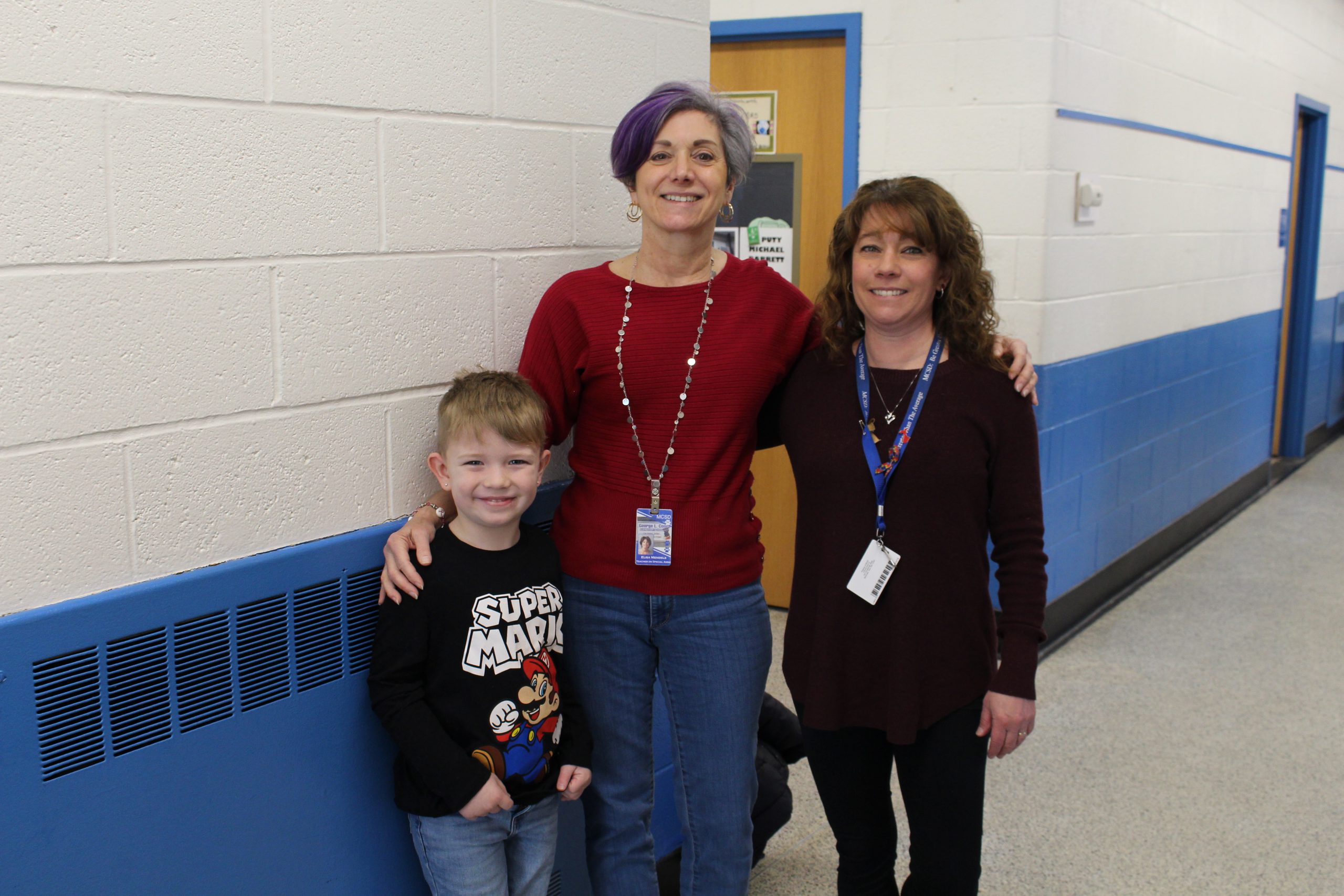 two women are smiling in a hallway and posing with a student