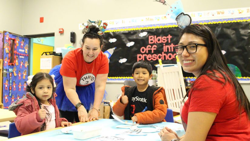 two students are seated at a table while two teachers help them.