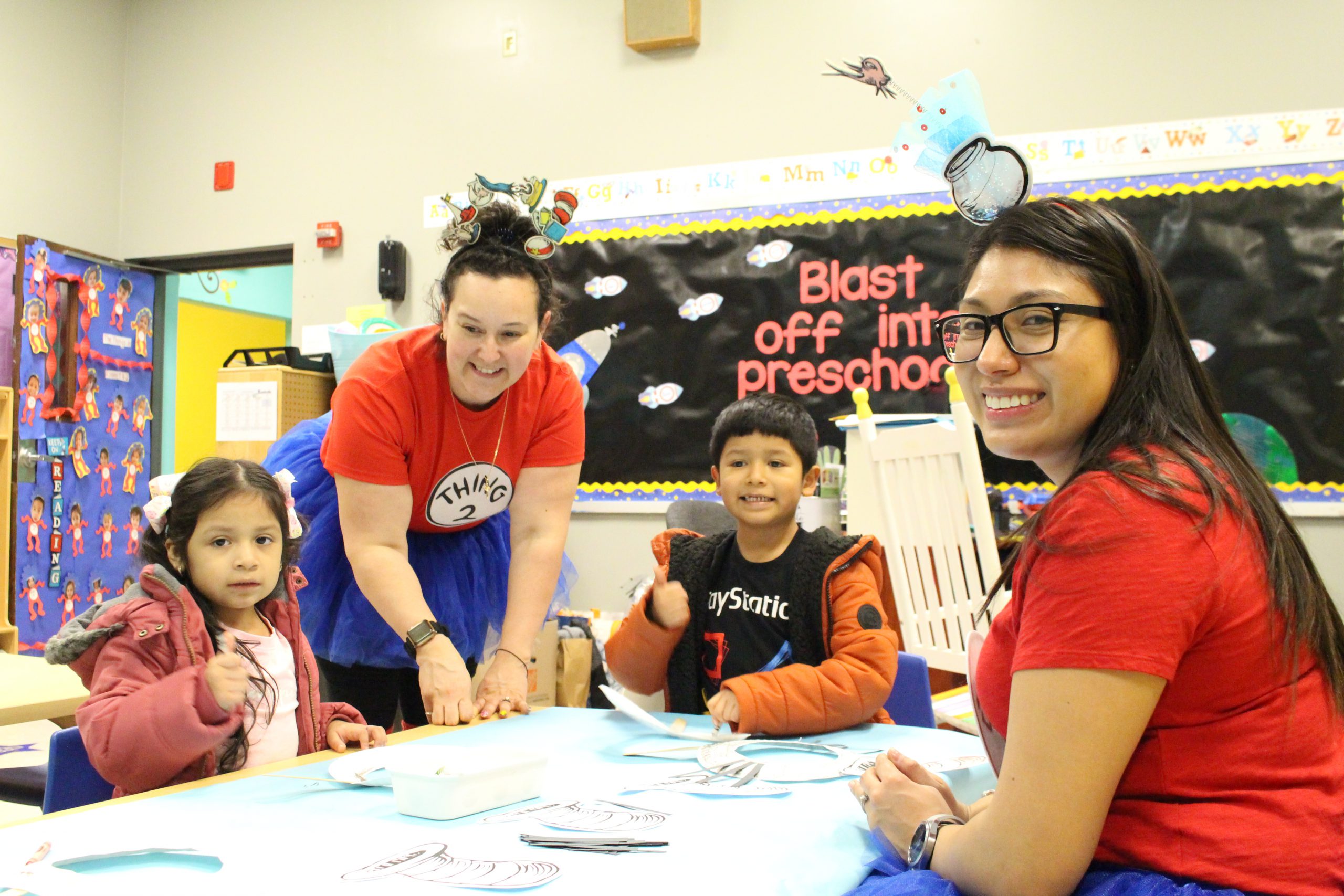 two students are seated at a table while two teachers help them. 