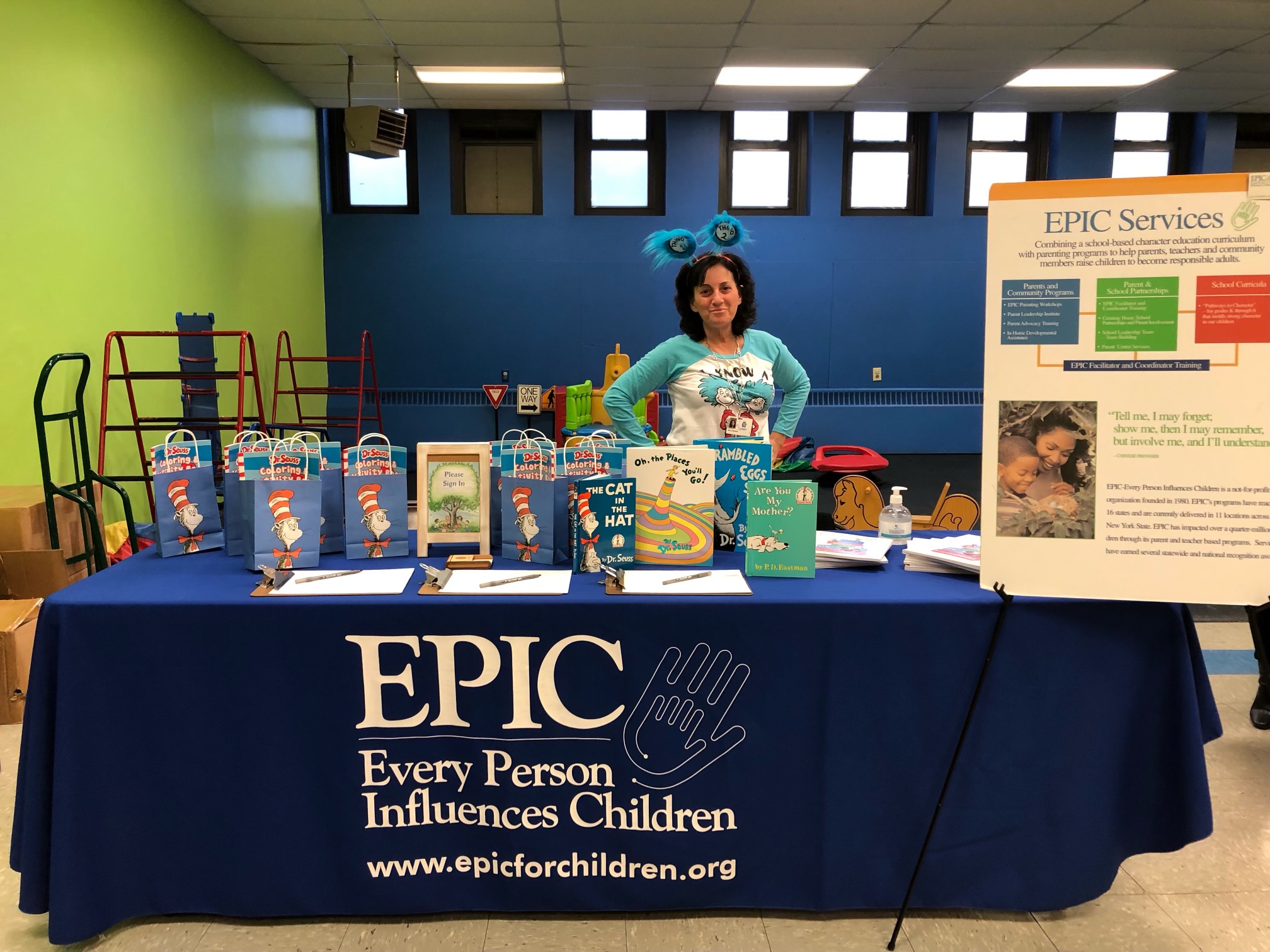 Jane Sorensen stands behind a table. There is a tablecloth on the table that reads EPIC and there are a variety of Dr. Seuss books. 
