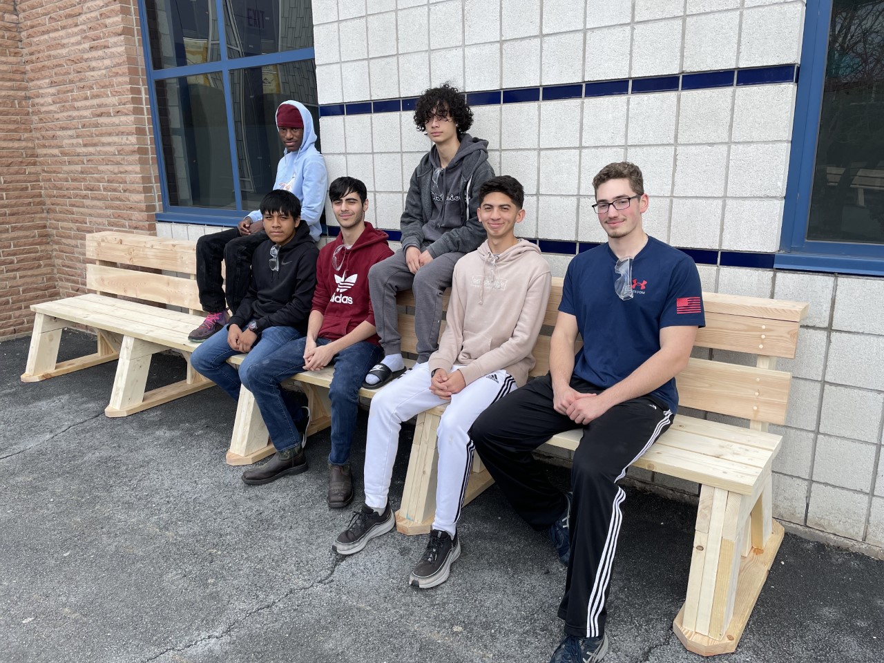 a large group of students are posing on a bench they made. 