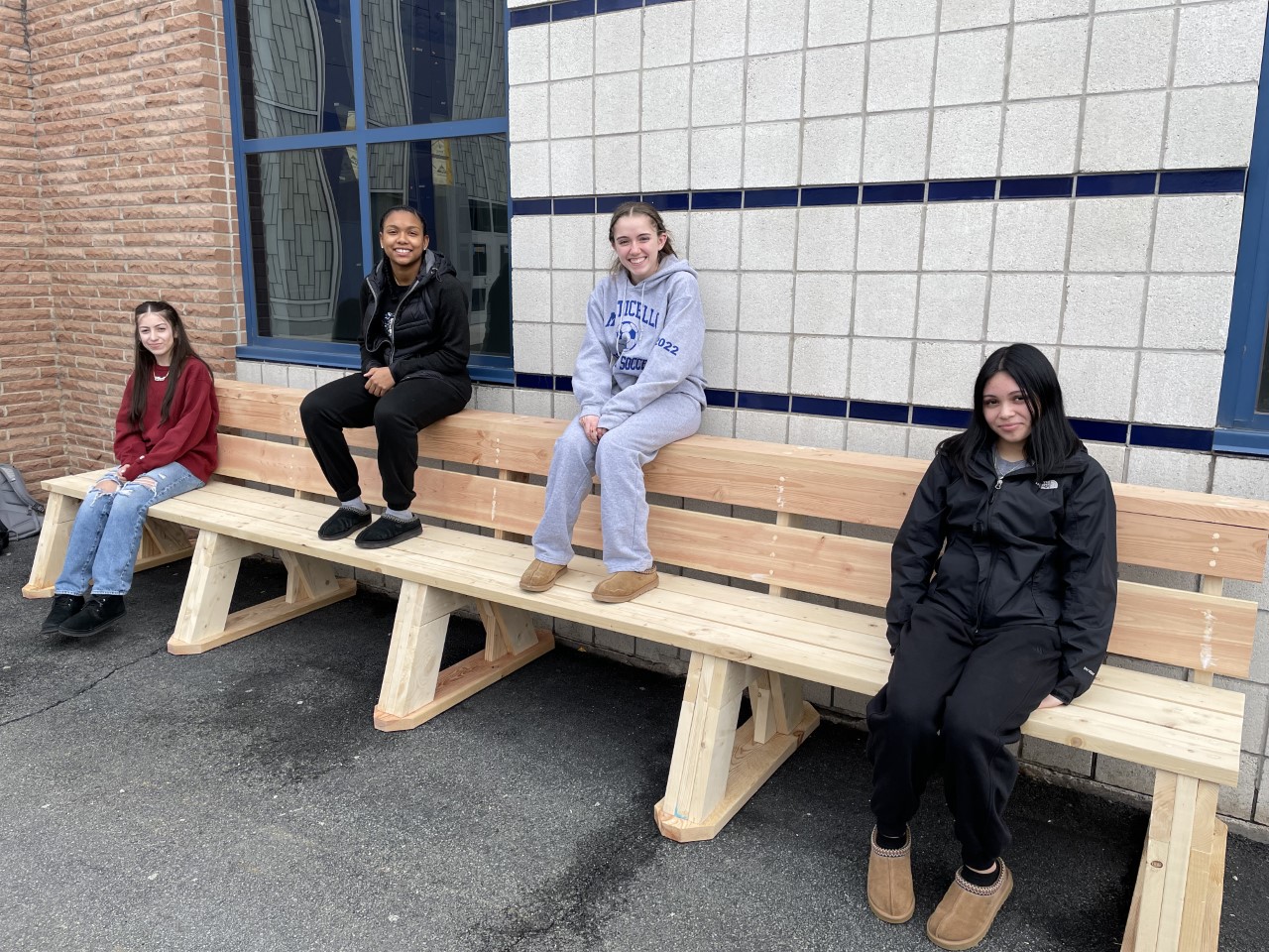 four students are posing on one of the benches they created 