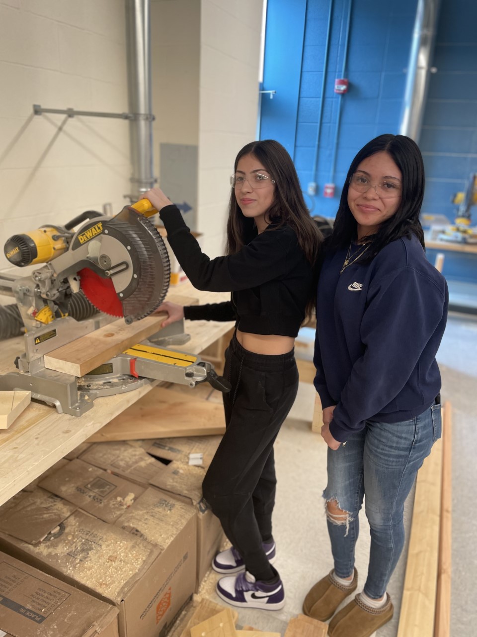 two female students are using a saw to cut wood