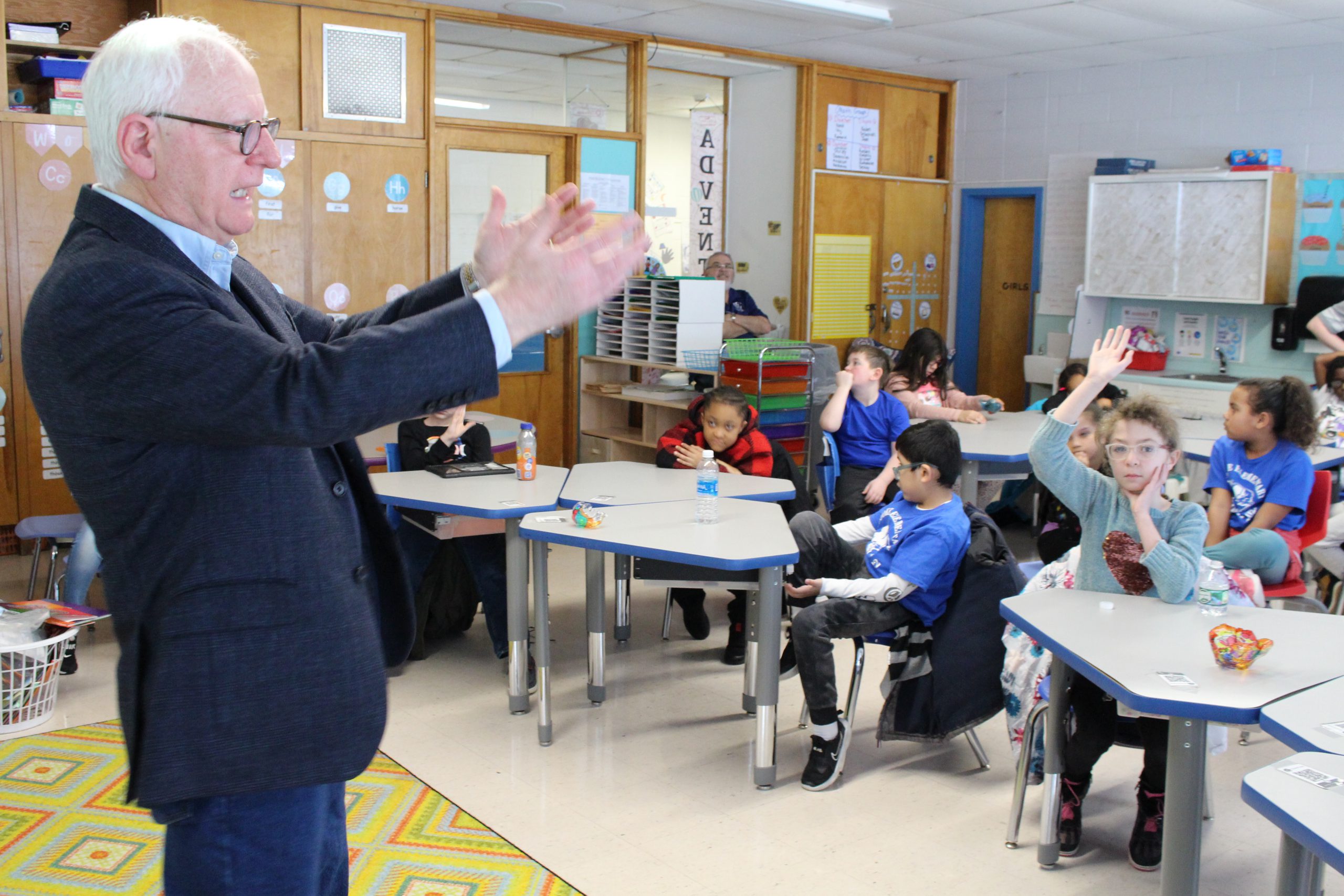 Mr. Conway is standing before a classroom of students. He has his hands out as if gesturing. The students are all seated at desks listening intently.