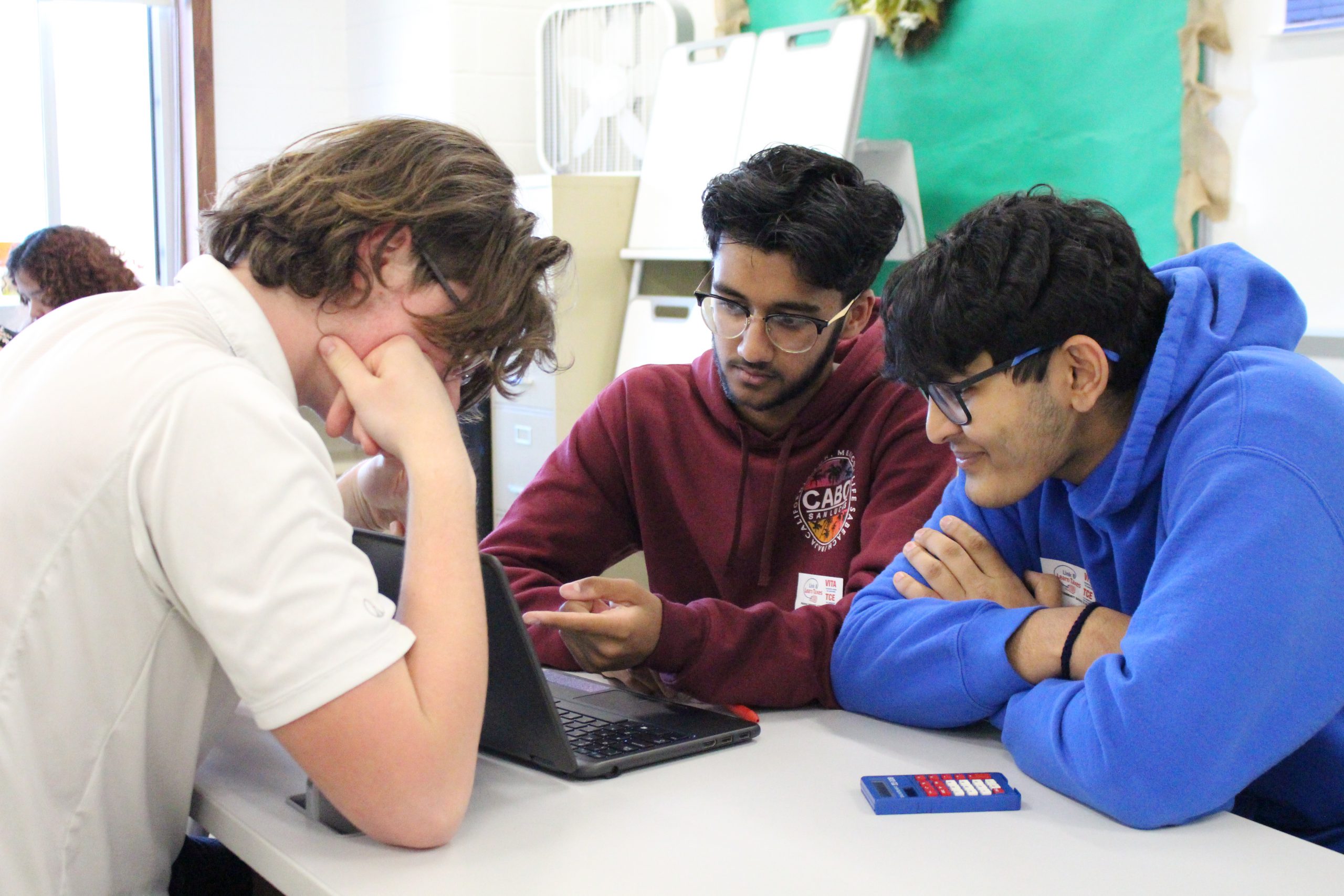 three students are huddled around a computer 