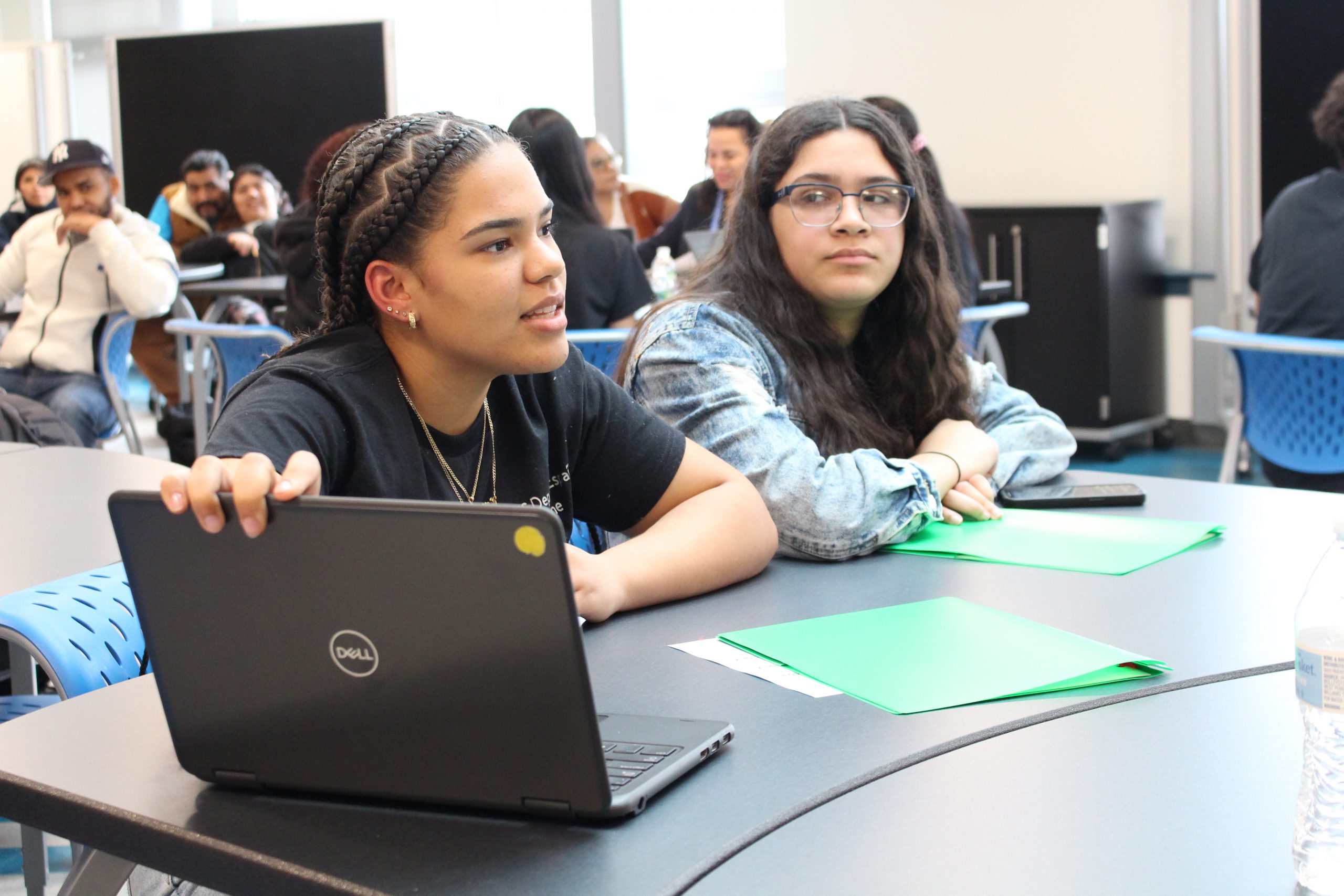 two female students are seated at a table in the middle of a conversation. 