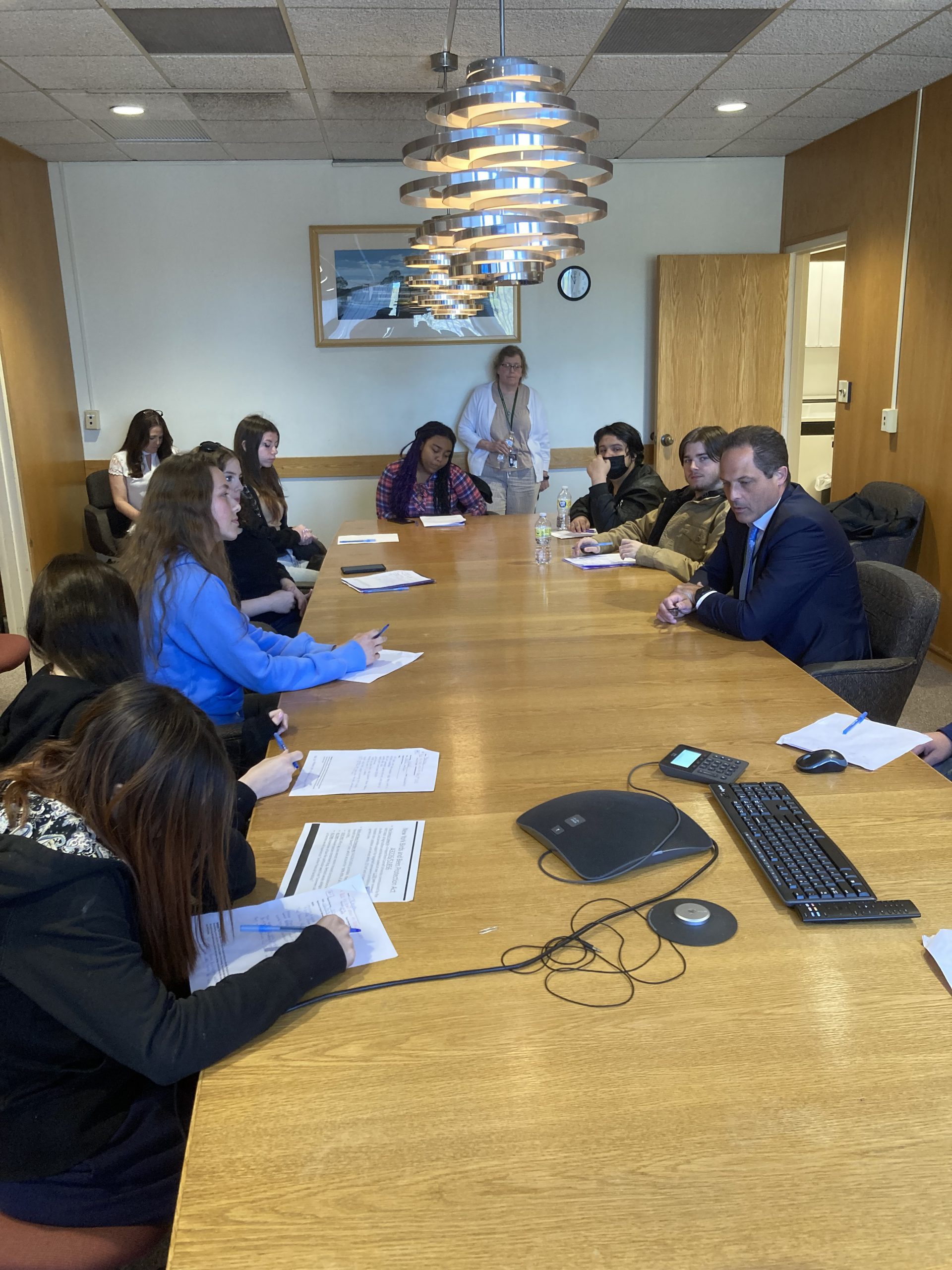 students are gathered around a long table in a board room 