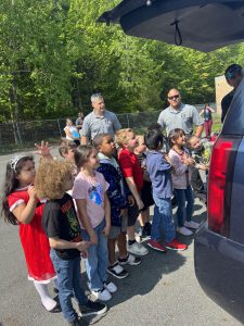 a group of students are listening to a police officer speak outdoors near a police car. 