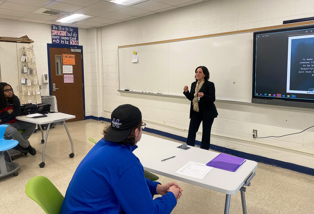 Woman speaking at the front of a classroom.