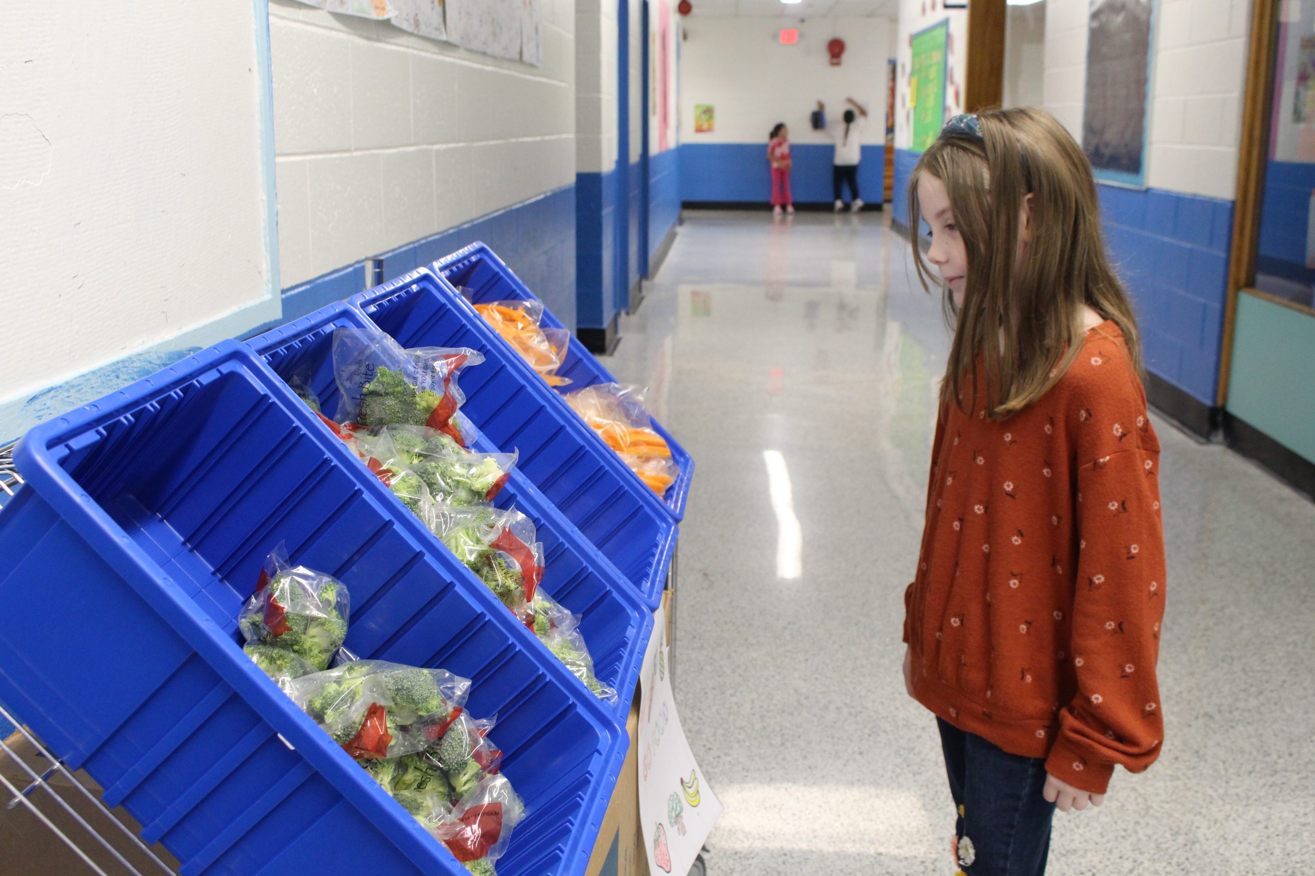a young girl is looking at fresh fruit and vegetables on a cart
