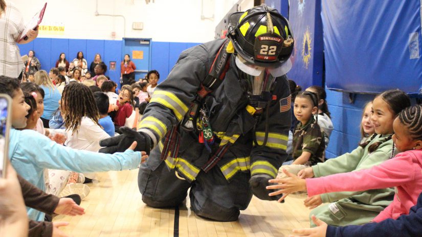 a firefighter is crawling on the ground in his gear and high-fiving students