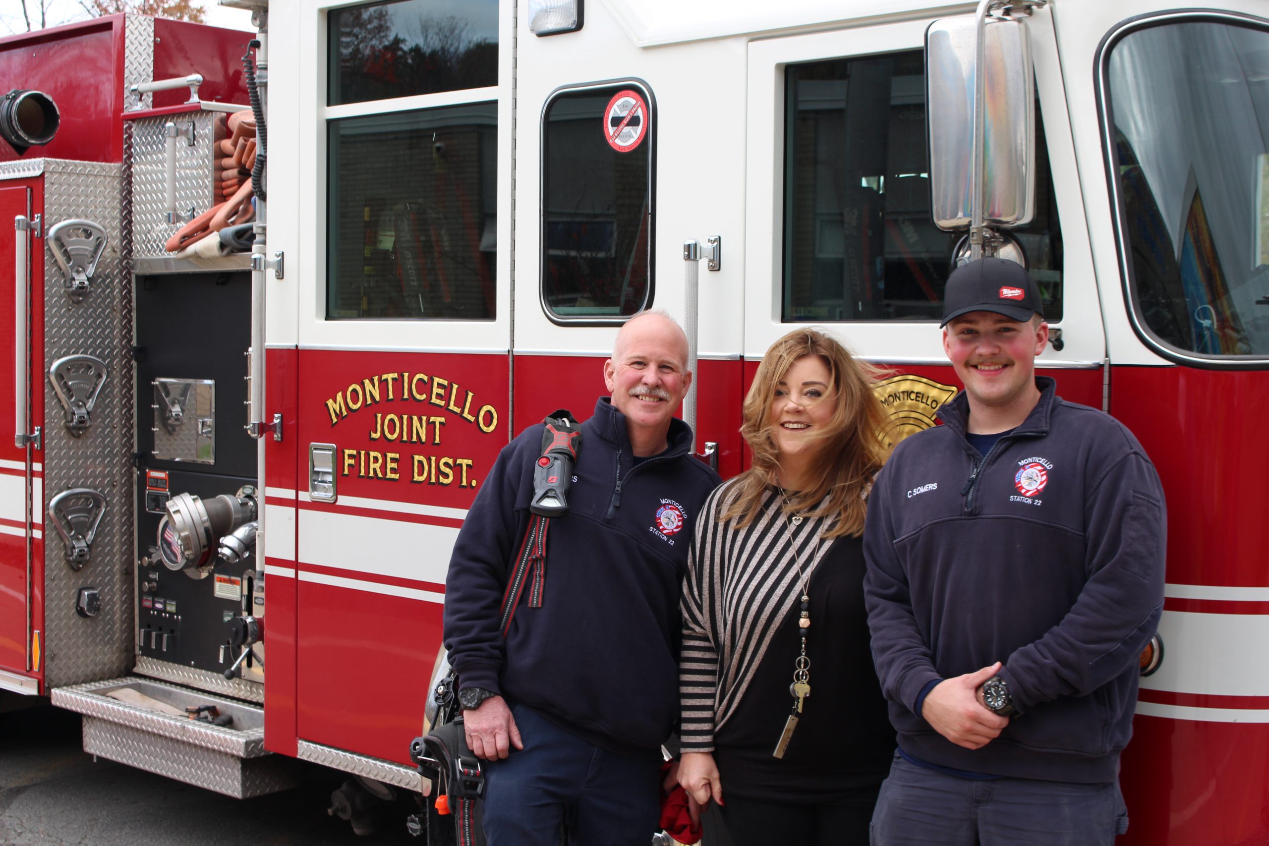 three people are posing in front of a fire truck 