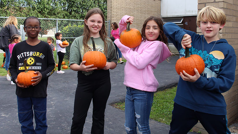 four students are holding up pumpkins