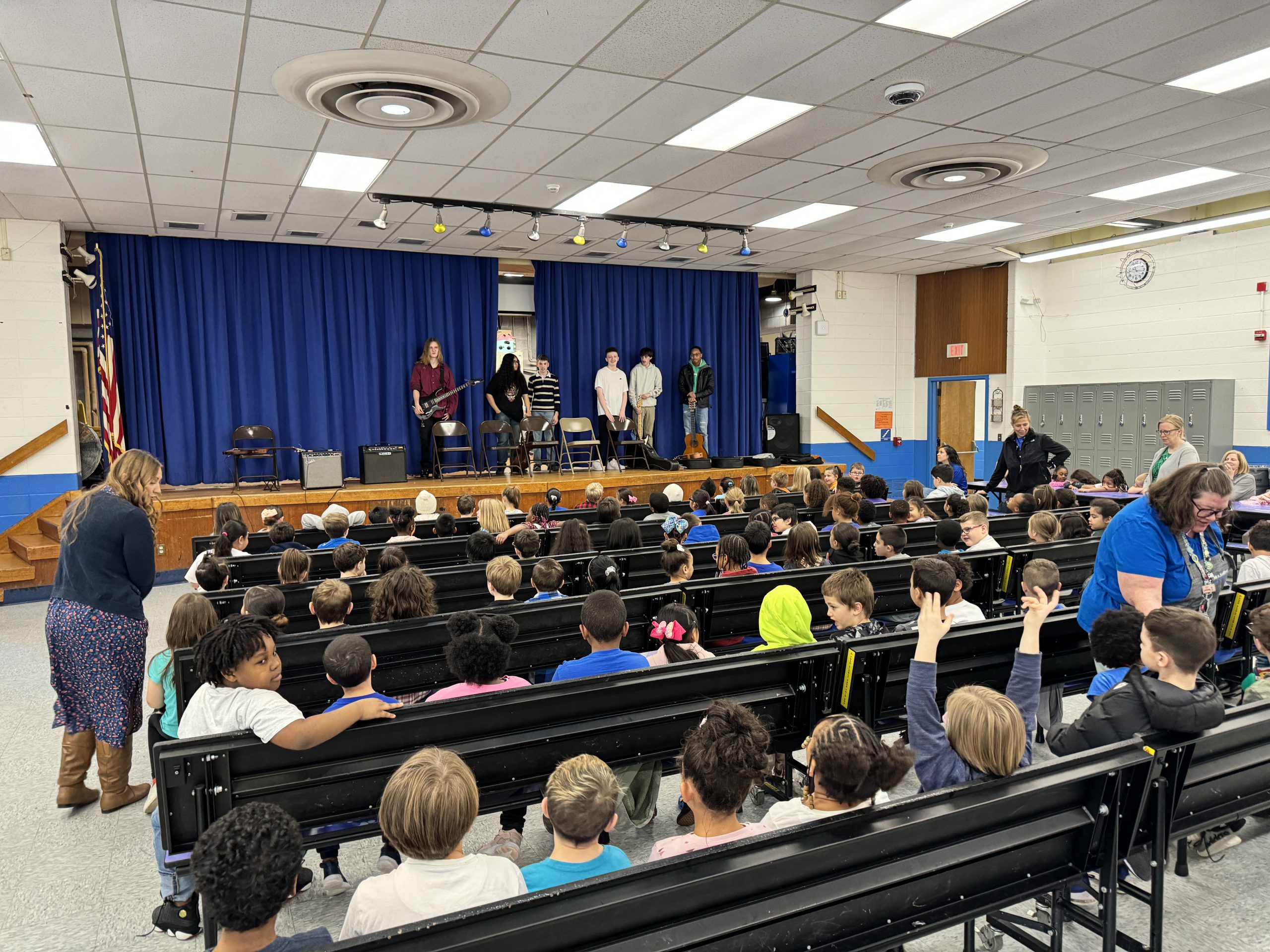 an audience full of students watches older students play guitar on stage. 