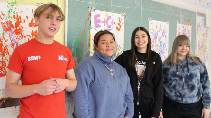 four students are posing in front of artwork they created