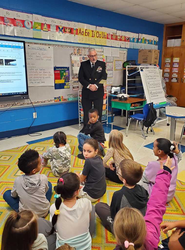 Man wearing a U.S. Navy uniform speaking to elementary students.