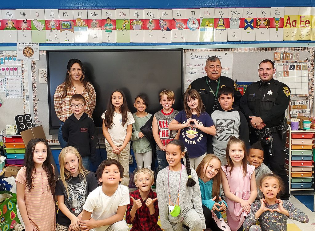 Three military service members smiling for a group photo with elementary students.