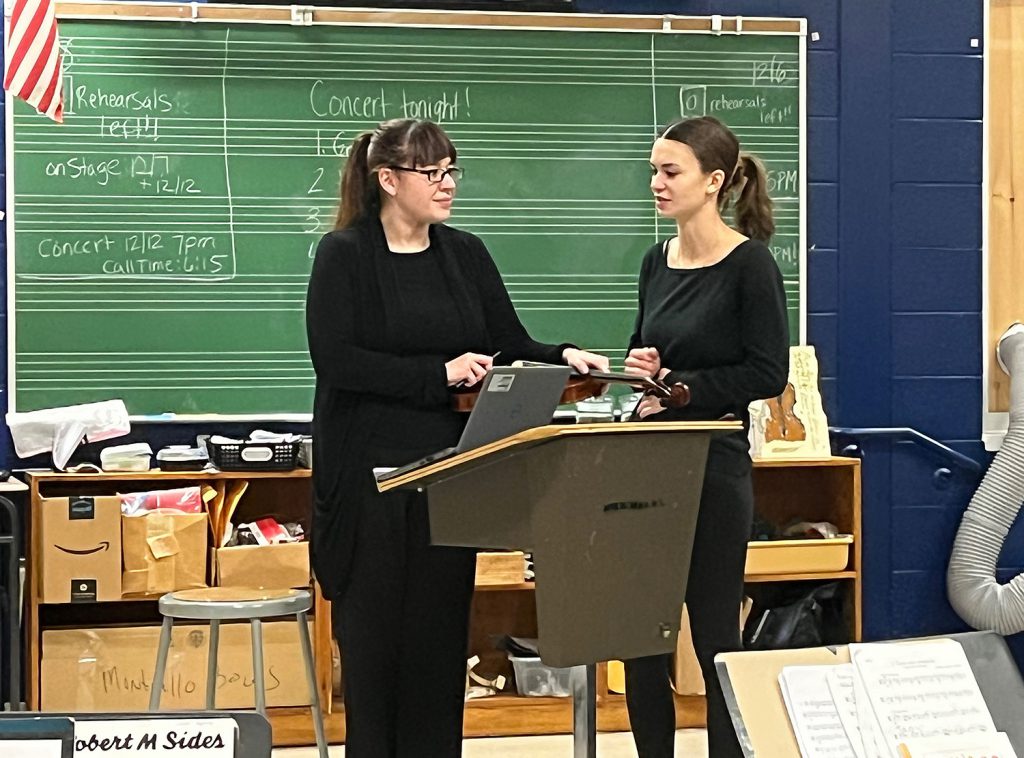 Music teacher and student talking by podium in a classroom.