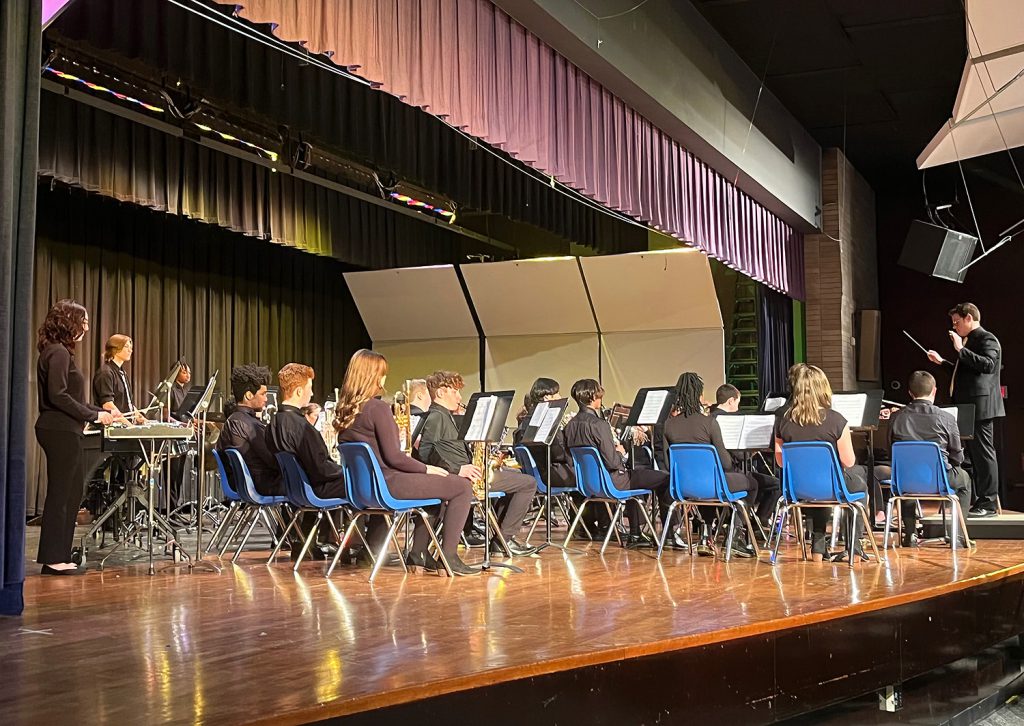 Student musicians sitting in chairs on stage, performing.
