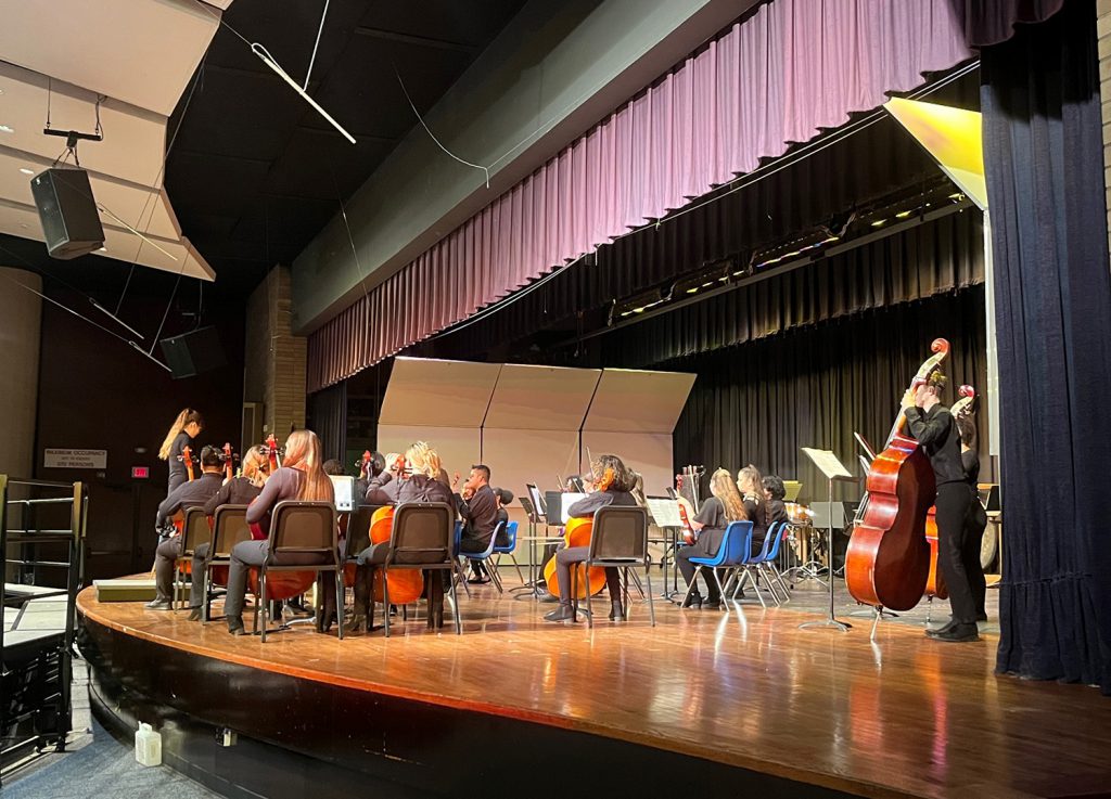 Students playing string instruments on stage.