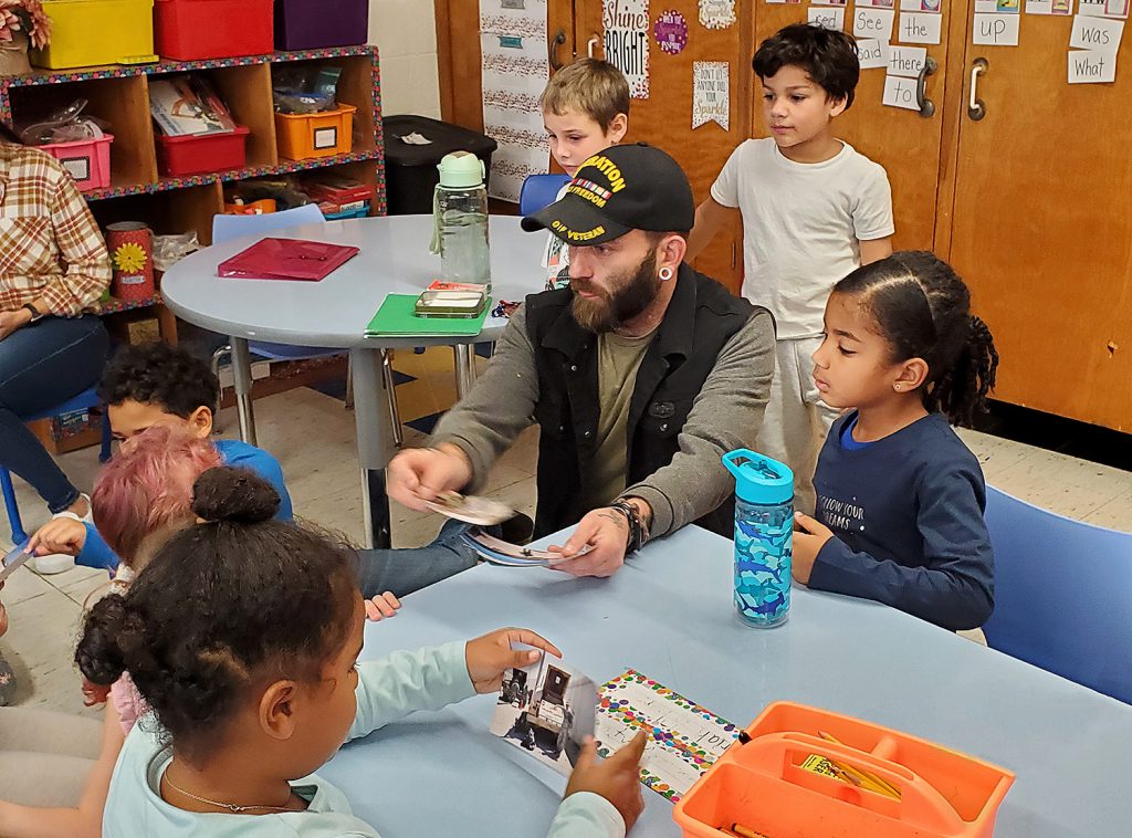 Man speaking to a group of elementary students at their table.
