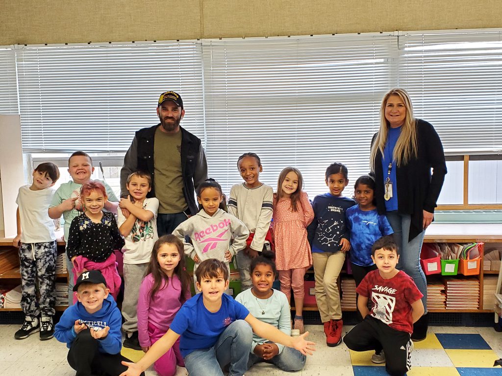 Man smiling for a group photo with an elementary teacher and her students.