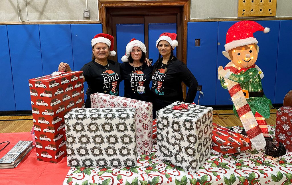 Three women smiling for a photo together with a table full of holiday gifts in front of them.