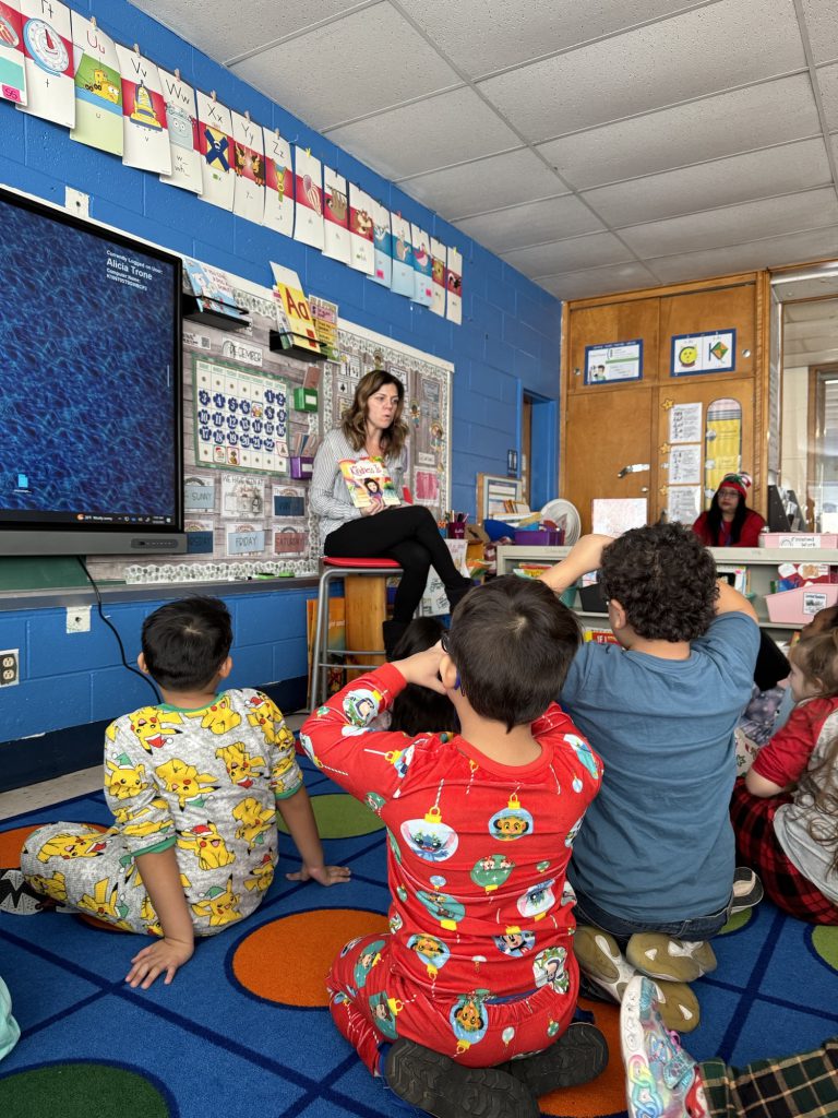 a teacher is seated at the head of the class and reading a story to her students
