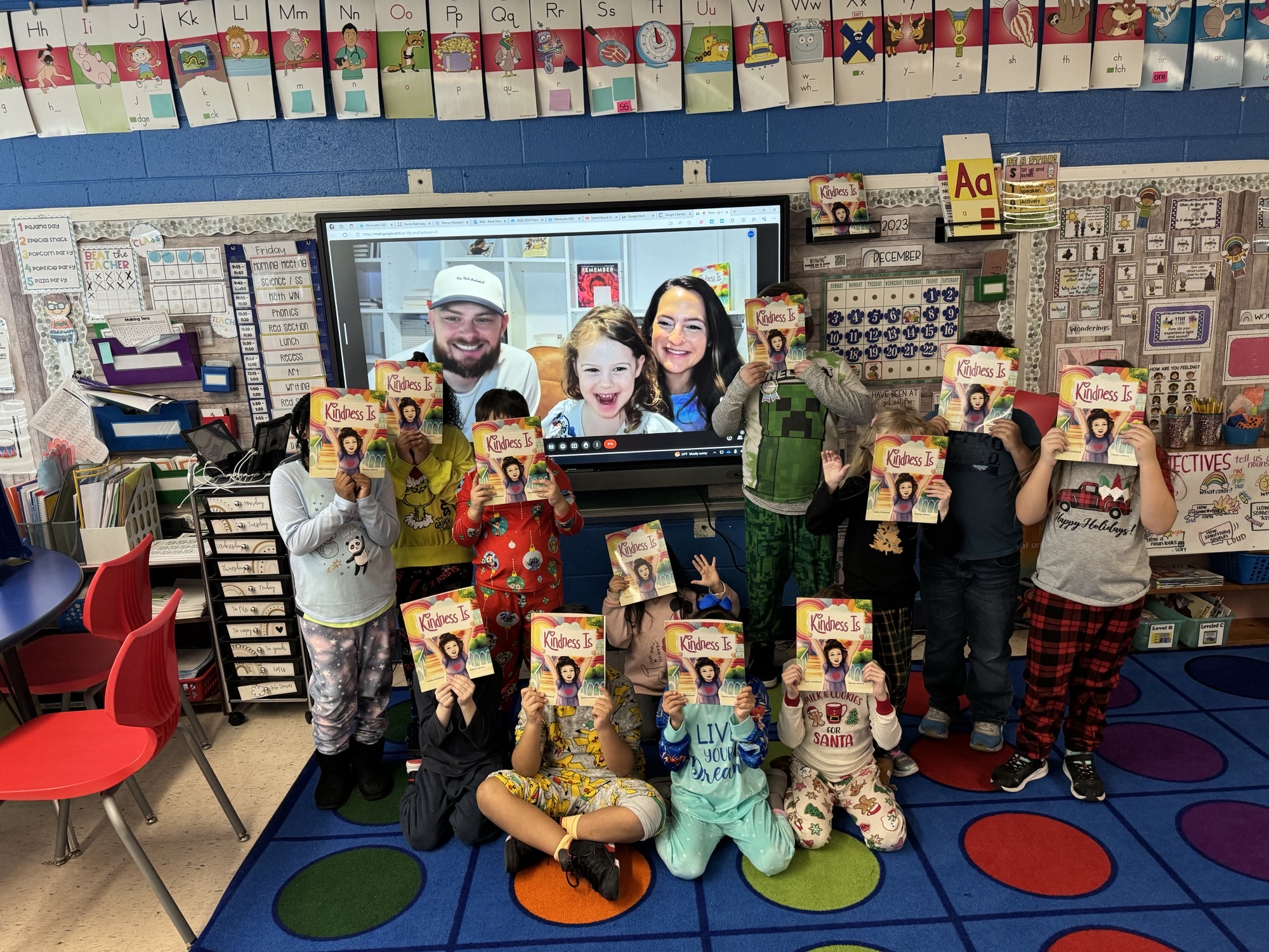 a group of students are posing and holding up copies of a book. In the background, there is a Zoom screen featuring the author, and her daughter and partner