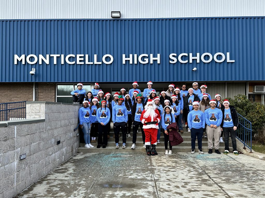 High school students and Santa Claus stand for a group photo in front of the exterior of Monticello High School.